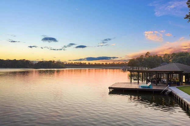Sunset over a calm lake with a wooden dock and a small gazebo on the right, reflecting warm colors on the water
